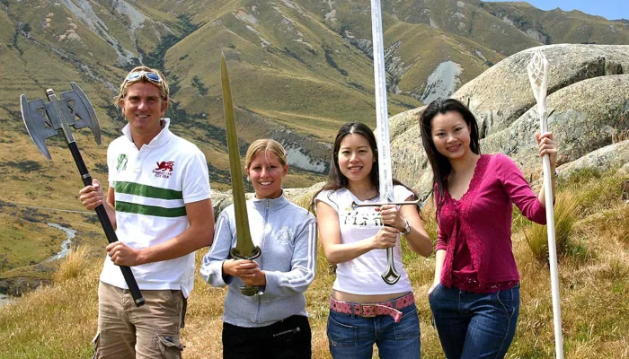 Group of four smiling guests each holding a different replica Lord of the Rings weapon in the high country.