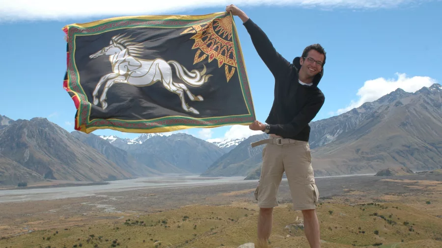 Smiling guest holding a Rohan flag with sweeping valley views near the Edoras filming site.
