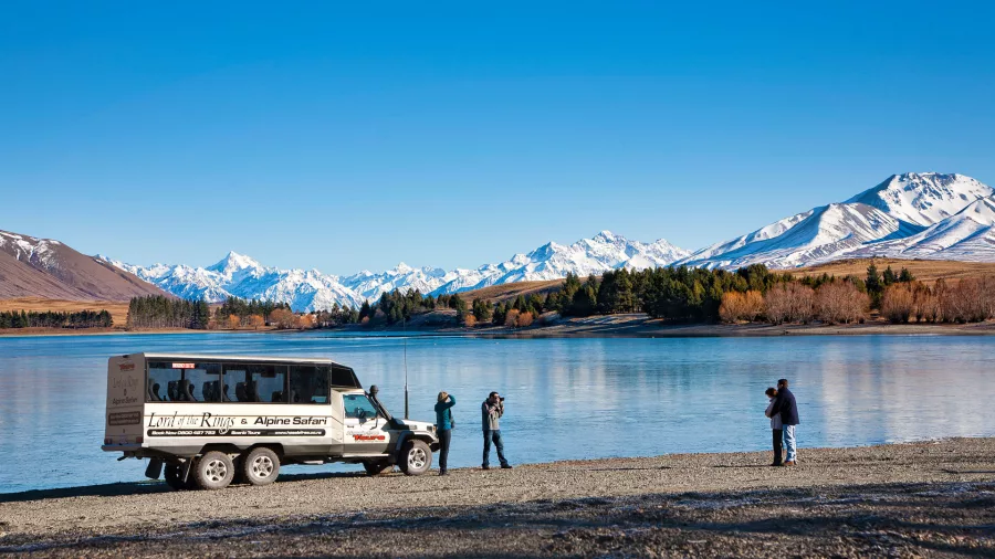 Alpine Safari vehicle parked by a lake with photographers capturing Aoraki/Mount Cook in the distance.