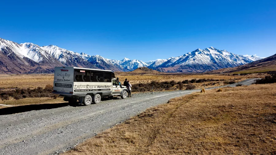 Tour vehicle parked on a gravel road with panoramic views of snow-covered peaks in the distance.