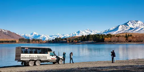 Alpine Safari vehicle parked by a lake with photographers capturing Aoraki/Mount Cook in the distance.