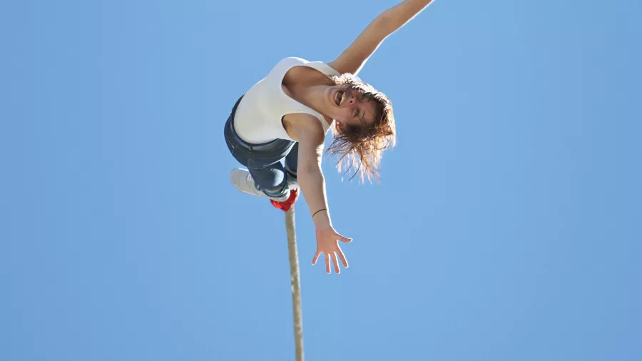 Woman mid-air during a bungy jump with arms outstretched against a vivid blue sky