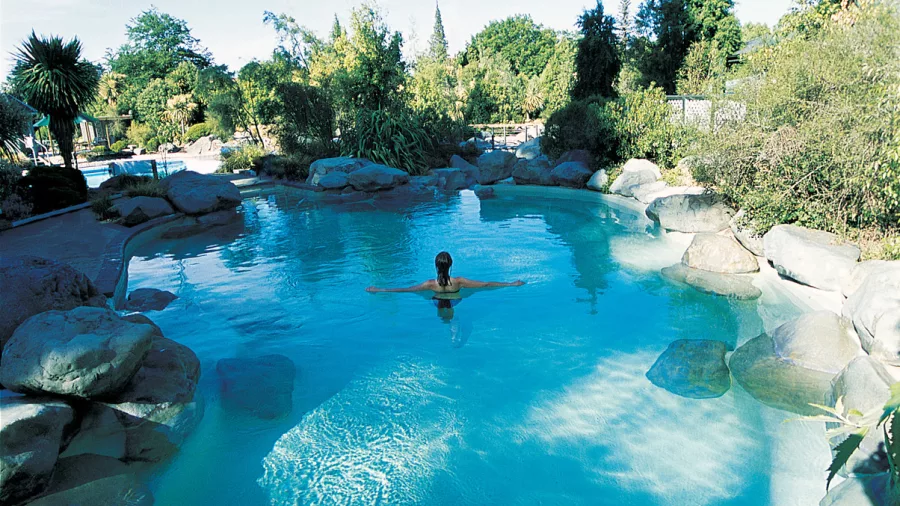 Person floating alone in a large turquoise thermal pool surrounded by lush greenery