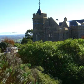 The historic Sign of the Takahe building in Christchurch, surrounded by lush greenery and blue skies.