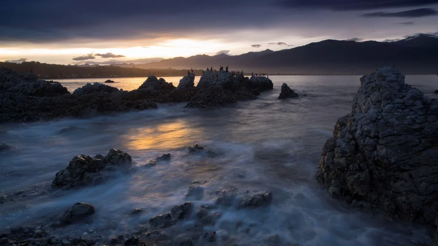 Sunset over Kaikōura coast with rugged rocks in the foreground