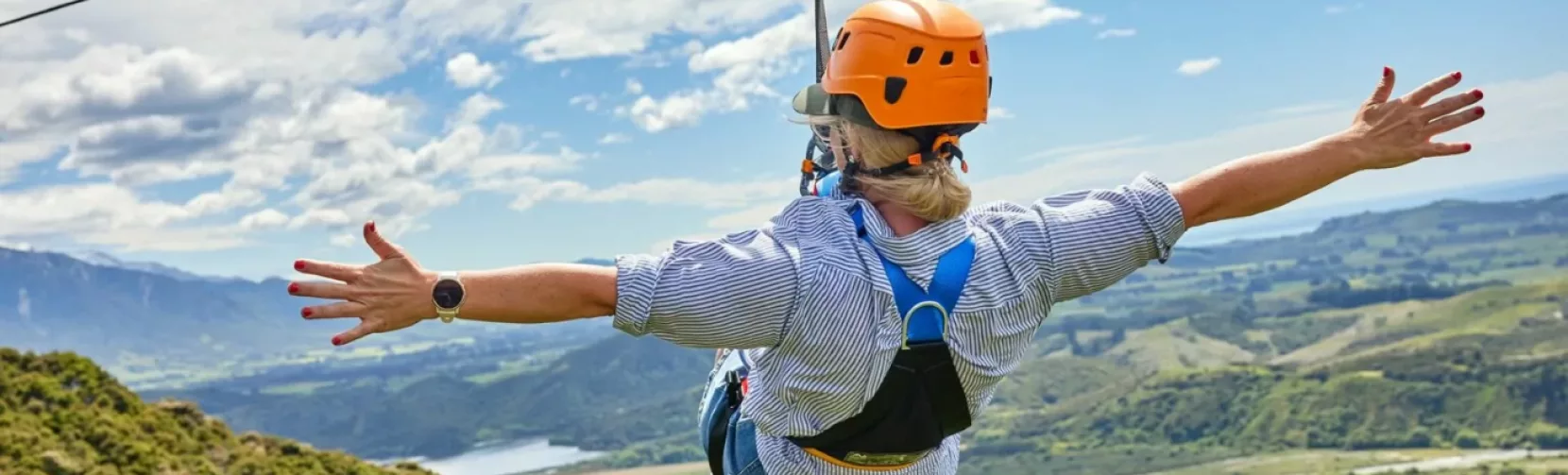 Solo zipliner rides with arms wide open above the Kaikōura countryside.