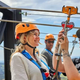 Smiling woman getting clipped into zipline harness by a guide in Kaikōura.
