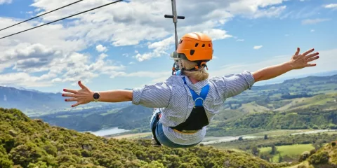 Solo zipliner rides with arms wide open above the Kaikōura countryside.