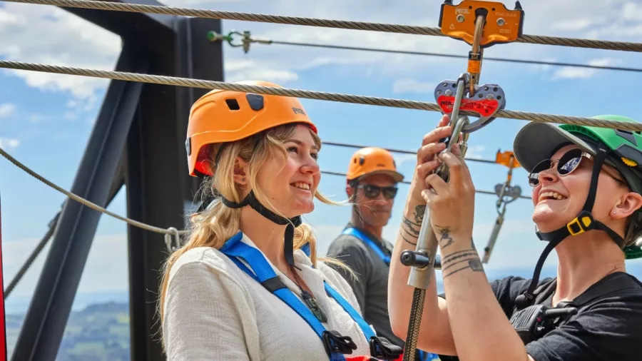 Smiling woman getting clipped into zipline harness by a guide in Kaikōura.