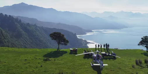 Group beside helicopter and ATVs on grassy hill overlooking Kaikōura’s dramatic coastline