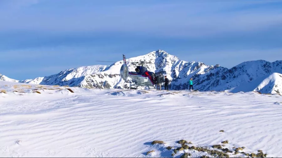 Guests standing by a helicopter after landing in a snowy clearing in the Kaikōura Ranges