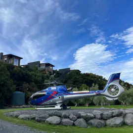 Hapuku Lodge and Kaikōura Helicopter under a bright blue sky with native garden