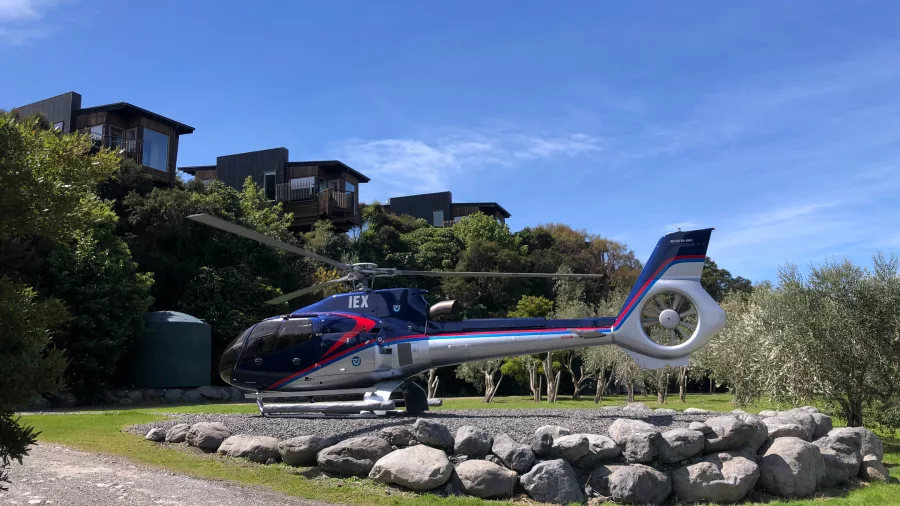Helicopter landed outside Hapuku Lodge surrounded by native greenery