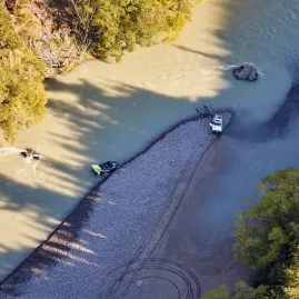 Aerial view of jet boat and 4x4 vehicle beside riverbed during Kaikōura Heli-Jet Adventure
