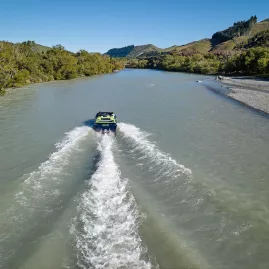 Back view of jet boat racing up the Hurunui River, creating a wide wake