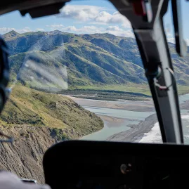 View from inside the helicopter flying along the Kaikōura coastline with mountains and ocean in sight