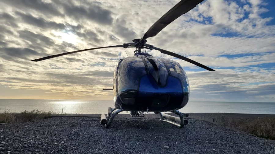 Helicopter parked near the coast with ocean and sunset in background