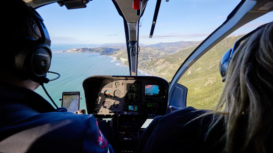 Helicopter cockpit view with pilot and passenger flying along the Kaikōura coast