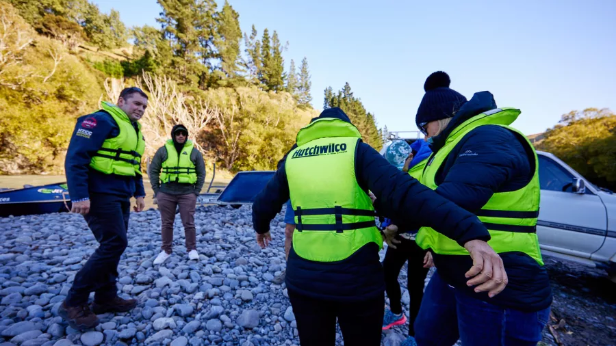 Guests getting ready for jet boating by putting on life jackets beside helicopter and 4x4