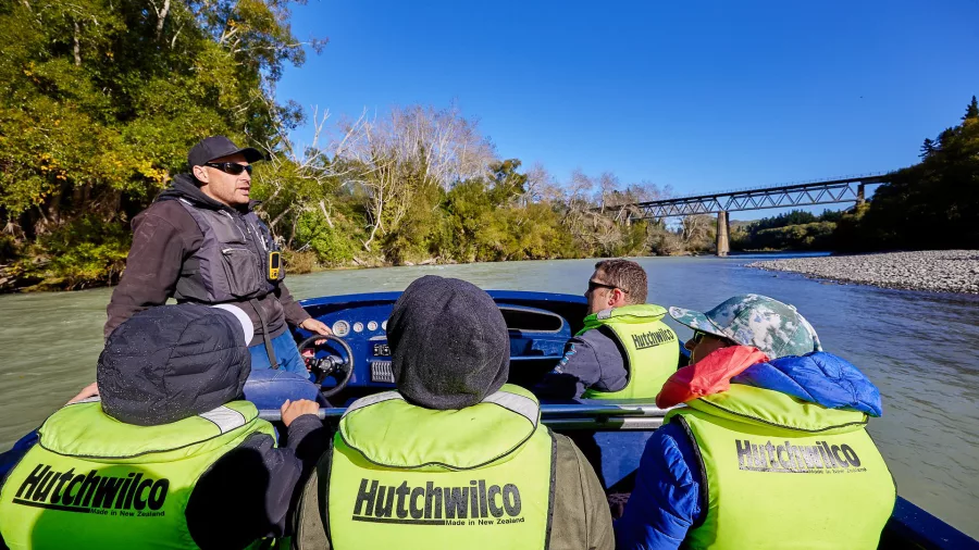 Jet boat passengers listening to guide with a historic bridge over the Hurunui River behind