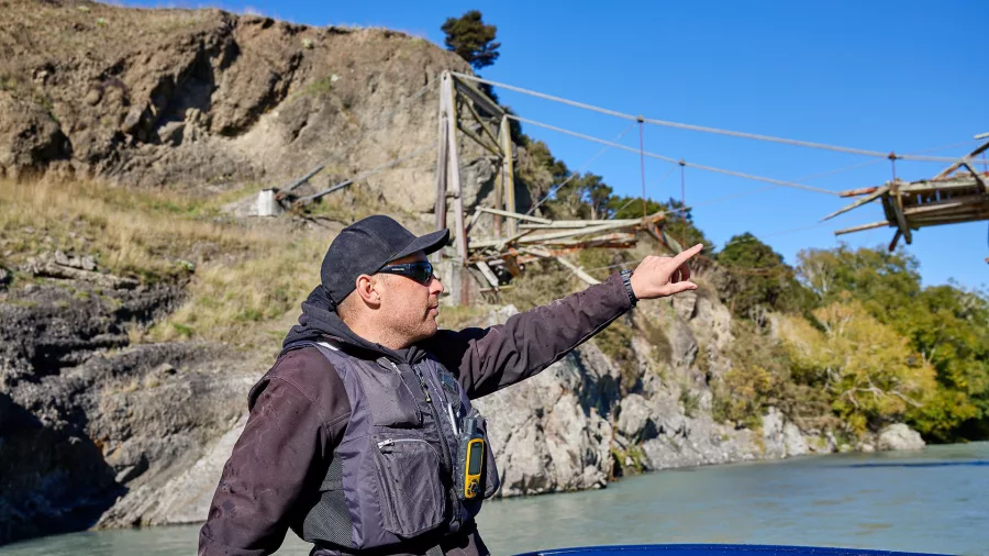 Jet boat guide pointing toward riverbank ruins and sharing local history in North Canterbury