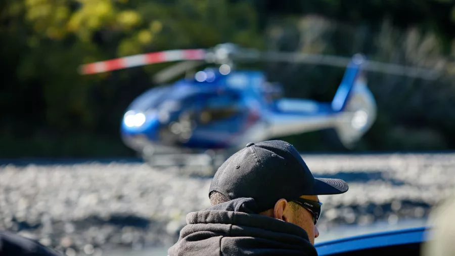 Man in cap watching helicopter landed on riverbed during Kaikōura Heli-Jet tour