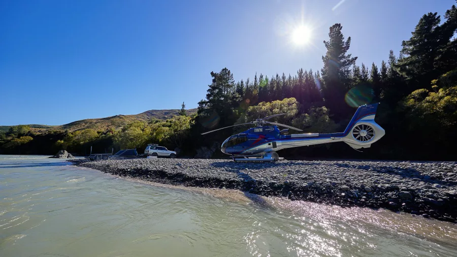 Helicopter parked on a stony riverbed under bright sun near Kaikōura during heli-jet adventure