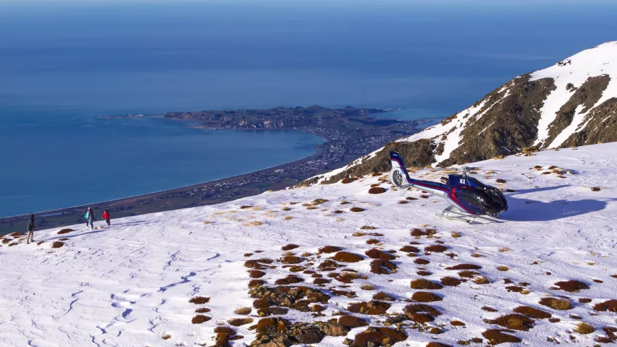 Helicopter landed in snow on Mt Fyffe with Kaikōura Peninsula and ocean in the distance