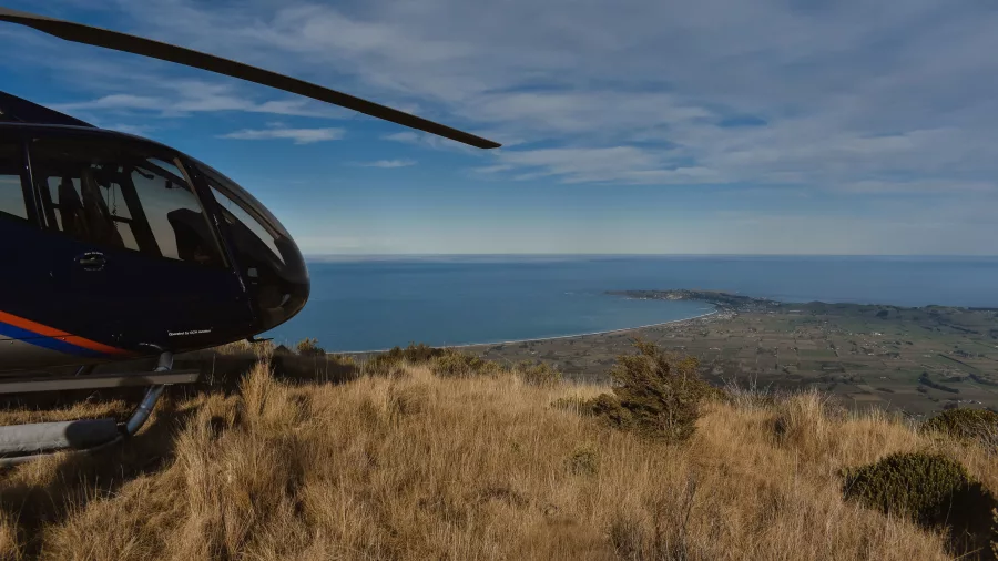 Helicopter parked on Mt Fyffe summit with ocean and Kaikōura township below
