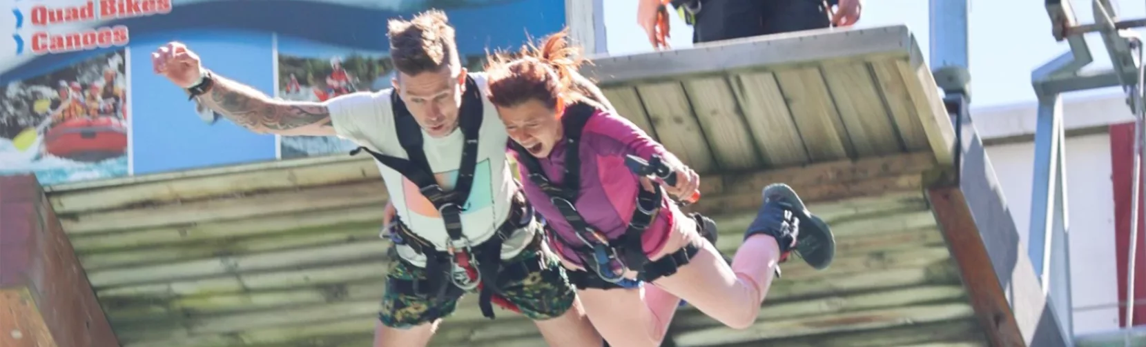 Couple jumping off the bungy platform with visible thrill-seekers signage in background
