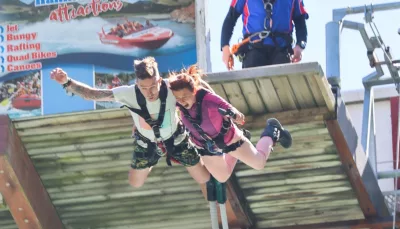 Couple jumping off the bungy platform with visible thrill-seekers signage in background