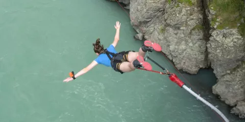 Woman in blue shirt jumping headfirst over the turquoise Waiau River