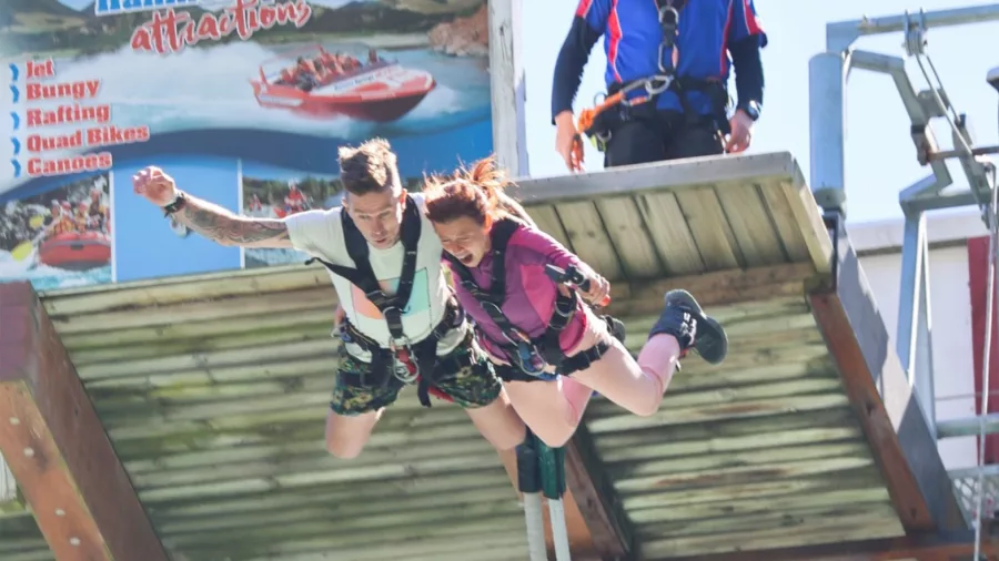Couple jumping off the bungy platform with visible thrill-seekers signage in background
