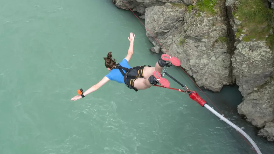 Woman in blue shirt jumping headfirst over the turquoise Waiau River