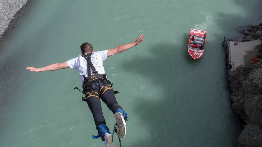 Man mid-jump over turquoise river with jet boat waiting below