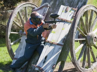 Man in full paintball gear using an old wooden cart as cover in Hanmer Springs