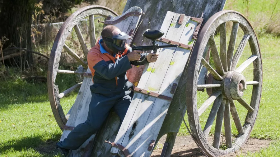 Man in full paintball gear using an old wooden cart as cover in Hanmer Springs