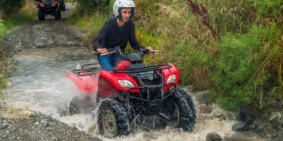 Young rider splashing through a shallow stream on a red quad bike in Hanmer Springs
