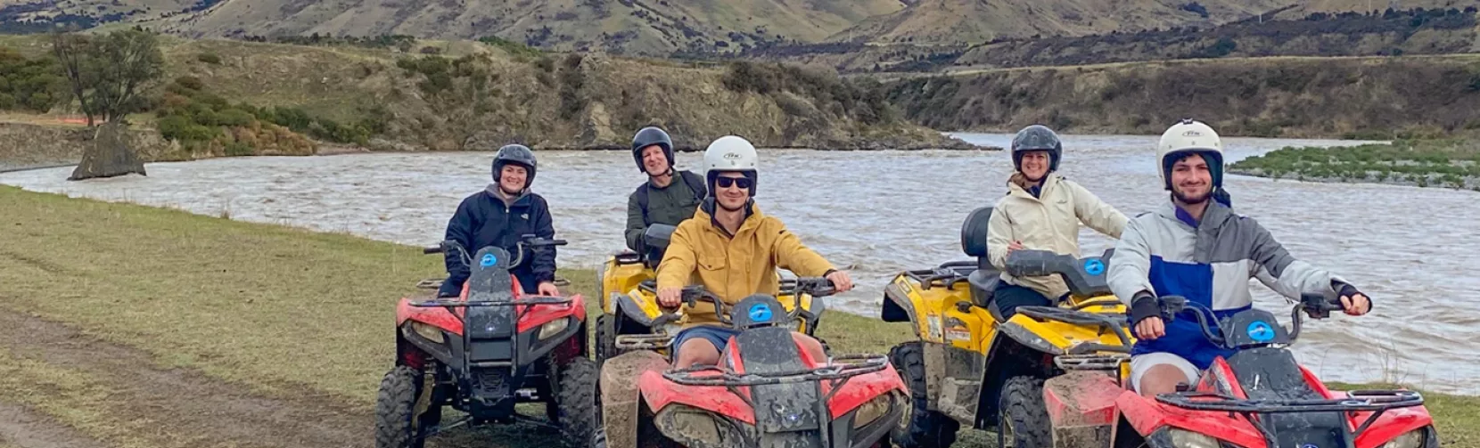 Group of quad bikers posing beside a river with mountain ranges in the background in Hanmer Springs