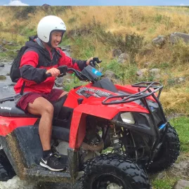 Man riding a red quad bike through a muddy track at Hanmer Springs, smiling mid-ride