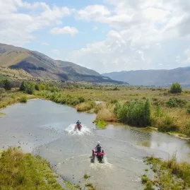 Two quad bikes splashing through a wetland trail in Hanmer Springs with dramatic mountains in the background