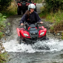 Woman riding a red quad bike through a rocky creek in Hanmer Springs with water splashing