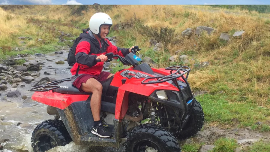 Man riding a red quad bike through a muddy track at Hanmer Springs, smiling mid-ride