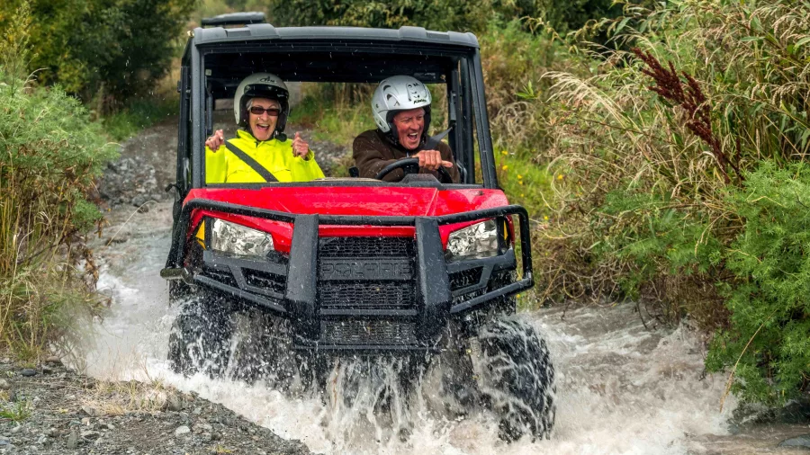 A couple riding a red off-road buggy splashing through a stream in Hanmer Springs