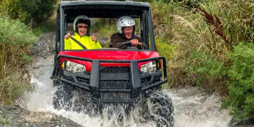 A couple riding a red off-road buggy splashing through a stream in Hanmer Springs