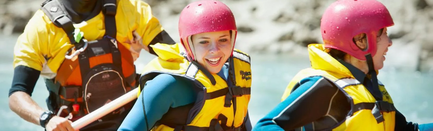 Close-up of smiling rafters in bright helmets and lifejackets enjoying the scenic ride in Hanmer Springs