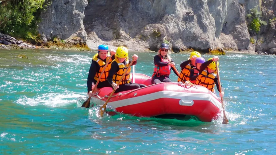 A family paddling together in a red raft led by a guide on a scenic river at Hanmer Springs Attractions