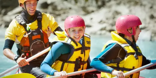 Close-up of smiling rafters in bright helmets and lifejackets enjoying the scenic ride in Hanmer Springs