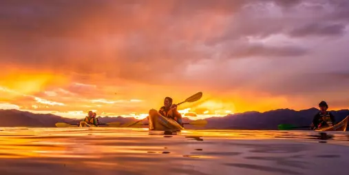 Group of kayakers on calm ocean waters under a dramatic sunset near Kaikōura, New Zealand
