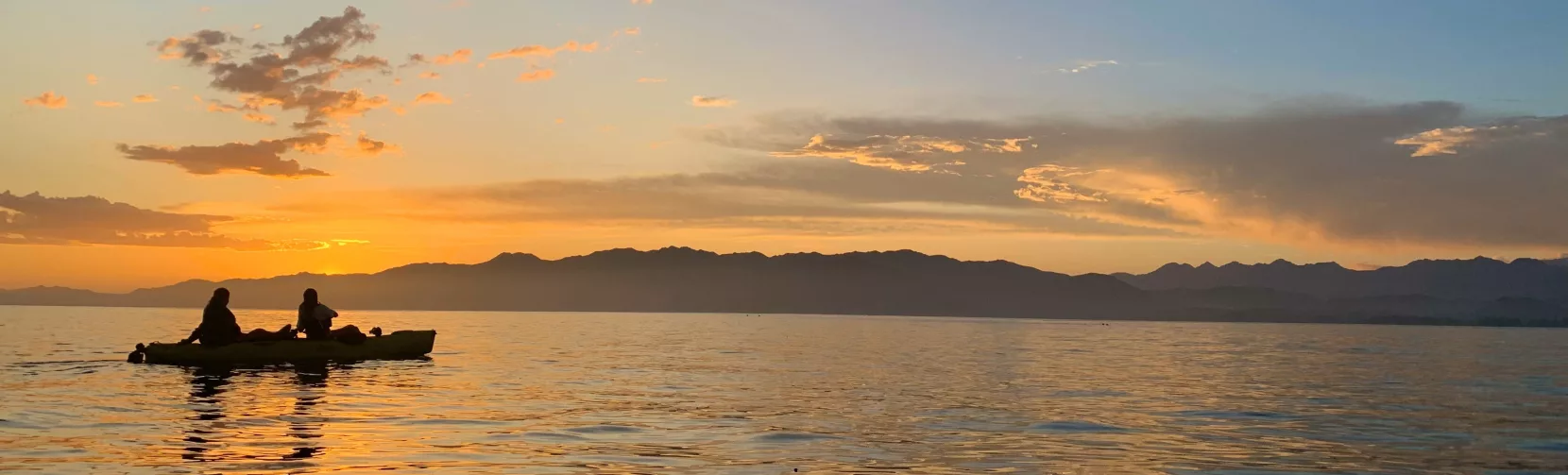 Two people kayaking on calm waters at sunset with the Kaikōura mountains in the distance